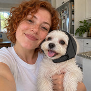 Selfie de una dueña con su perro blanco usando orejeras acolchadas
